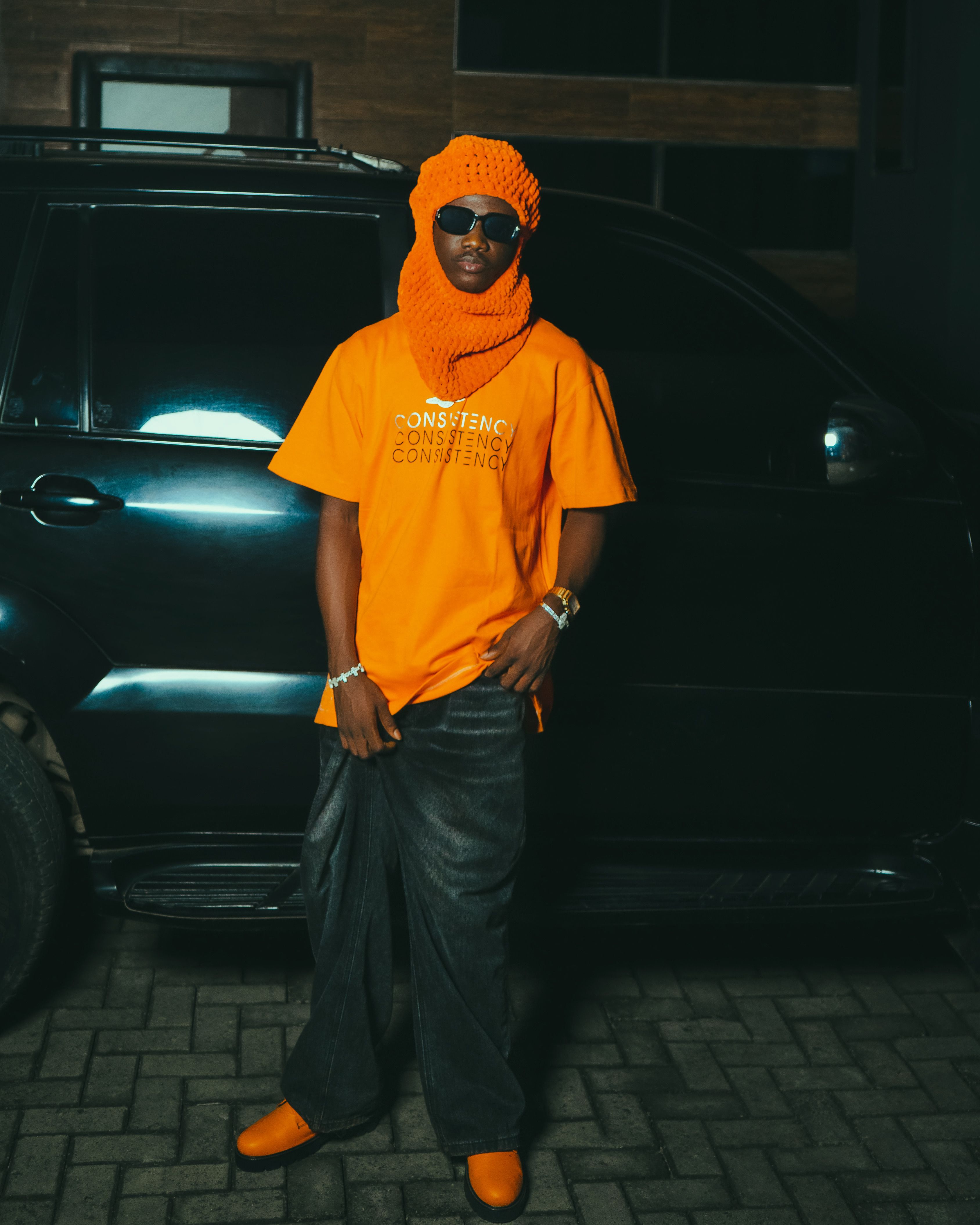 Stylish person in bold orange outfit standing confidently outdoors by a car.