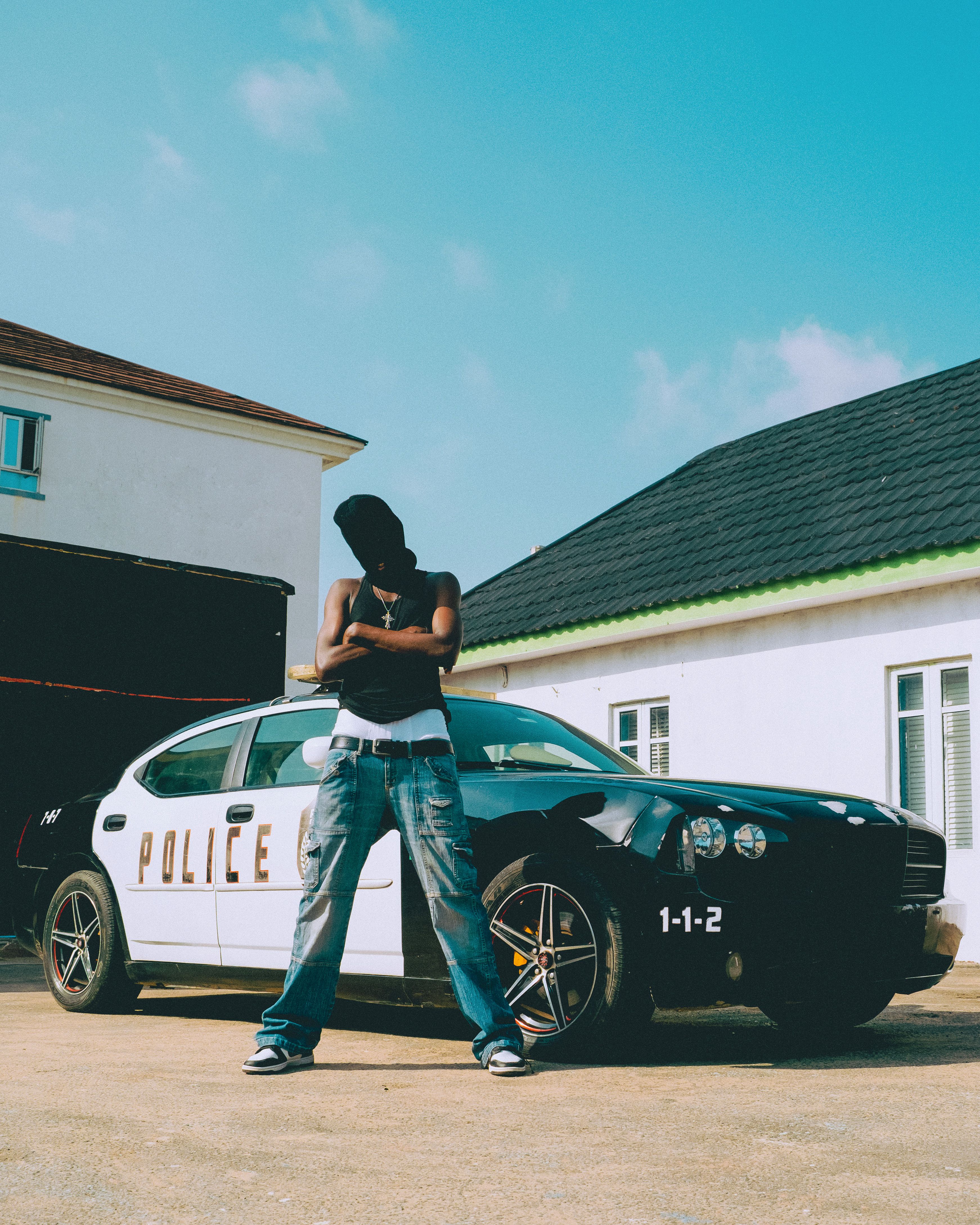 Man posing confidently next to vintage police car with building background, daytime.