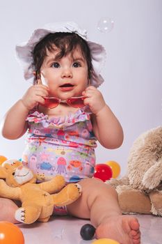 Adorable baby girl wearing a summer hat playing with colorful toys indoors.