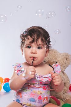 Cute baby playing with glasses surrounded by colorful bubbles and toys.