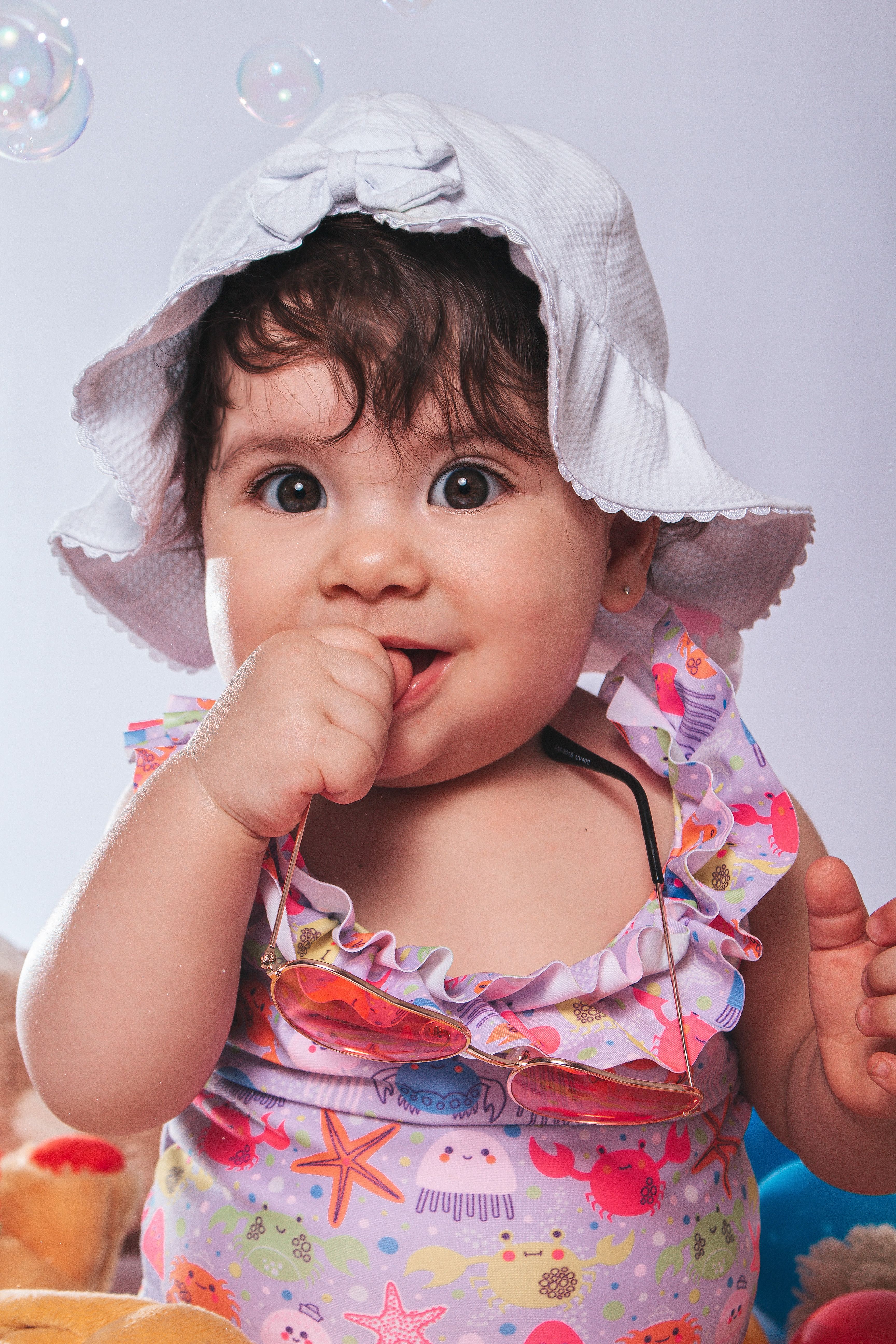 Cute baby in a hat, colorful outfit, surrounded by bubbles, capturing playful innocence.