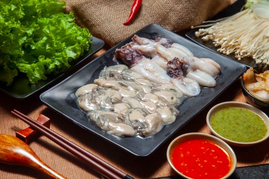 A delicious seafood platter featuring fresh oysters and squid with sauces and greens, perfect for gourmets.