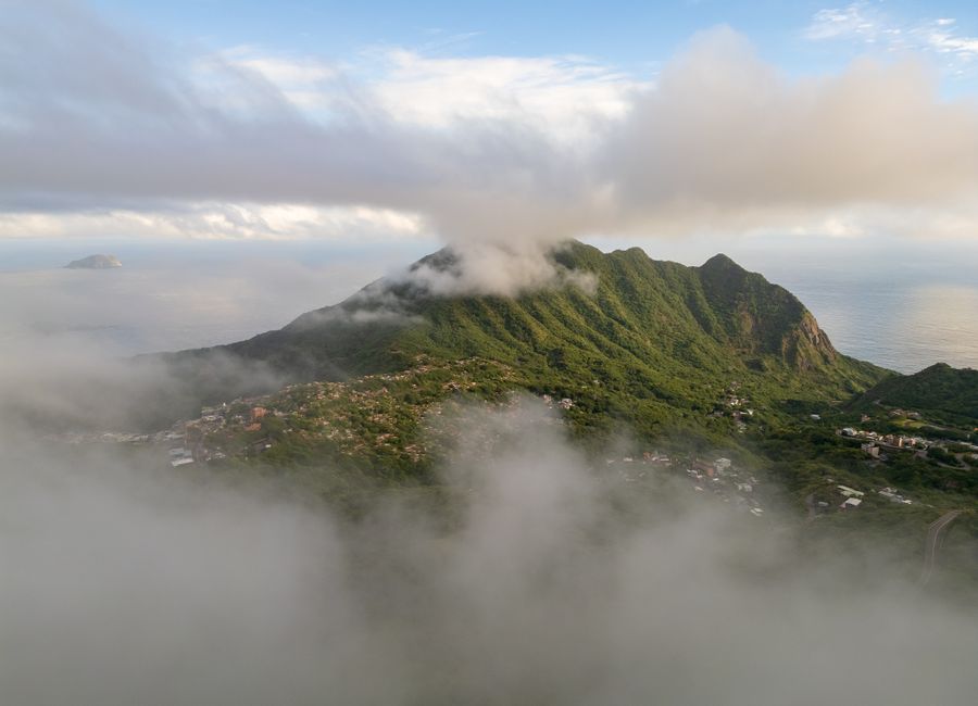 Breathtaking aerial shot of a cloud-covered mountain and coastal scenery during the day.