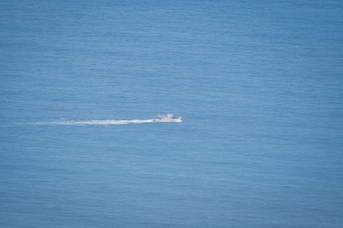 Free A lone boat travels over the expansive and calm blue ocean horizon. Stock Photo