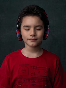 A young boy in a red shirt enjoying music with headphones.
