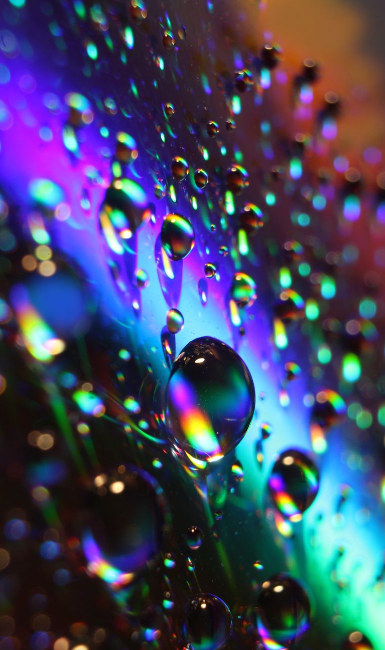Colorful close-up of water droplets reflecting light on a glass surface, creating a mesmerizing abstract pattern.