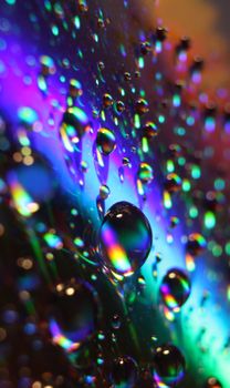 Colorful close-up of water droplets reflecting light on a glass surface, creating a mesmerizing abstract pattern.
