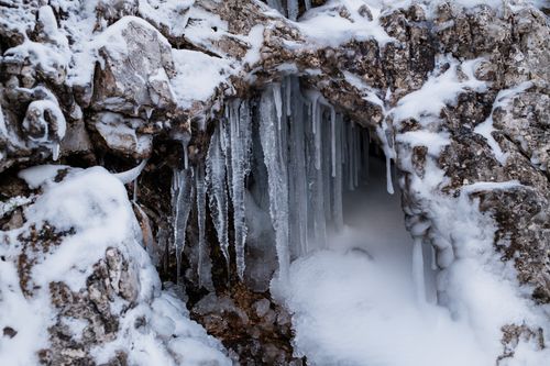 Free Close-up of icicles forming on a snow-covered rocky arch, showcasing winter's cold beauty. Stock Photo