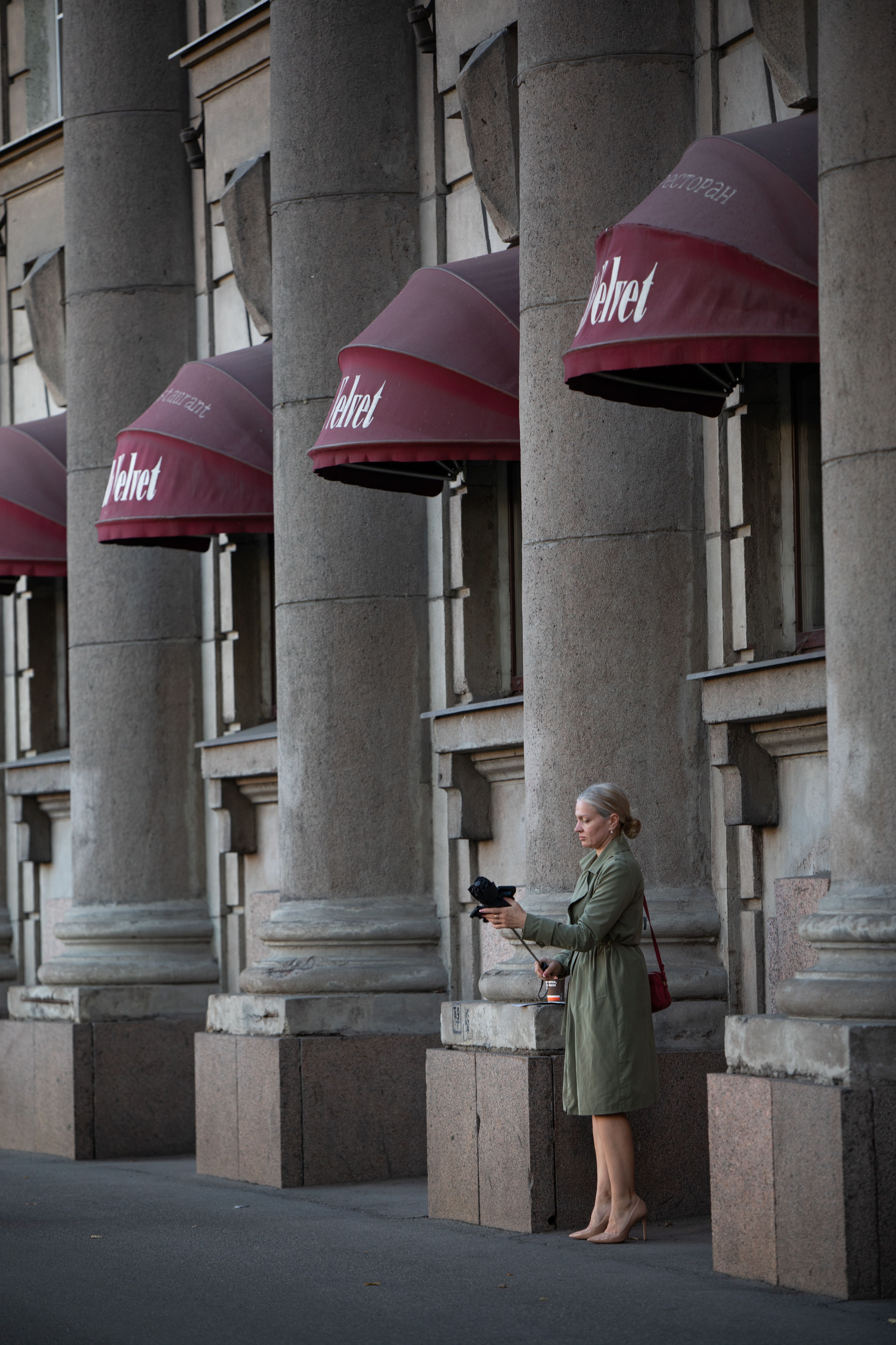 Stylish woman standing by grand building with red awnings, using a tablet. Urban lifestyle concept.