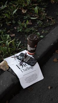 Disposable coffee cup and magazine on a sidewalk amidst grass, showcasing street vibes.