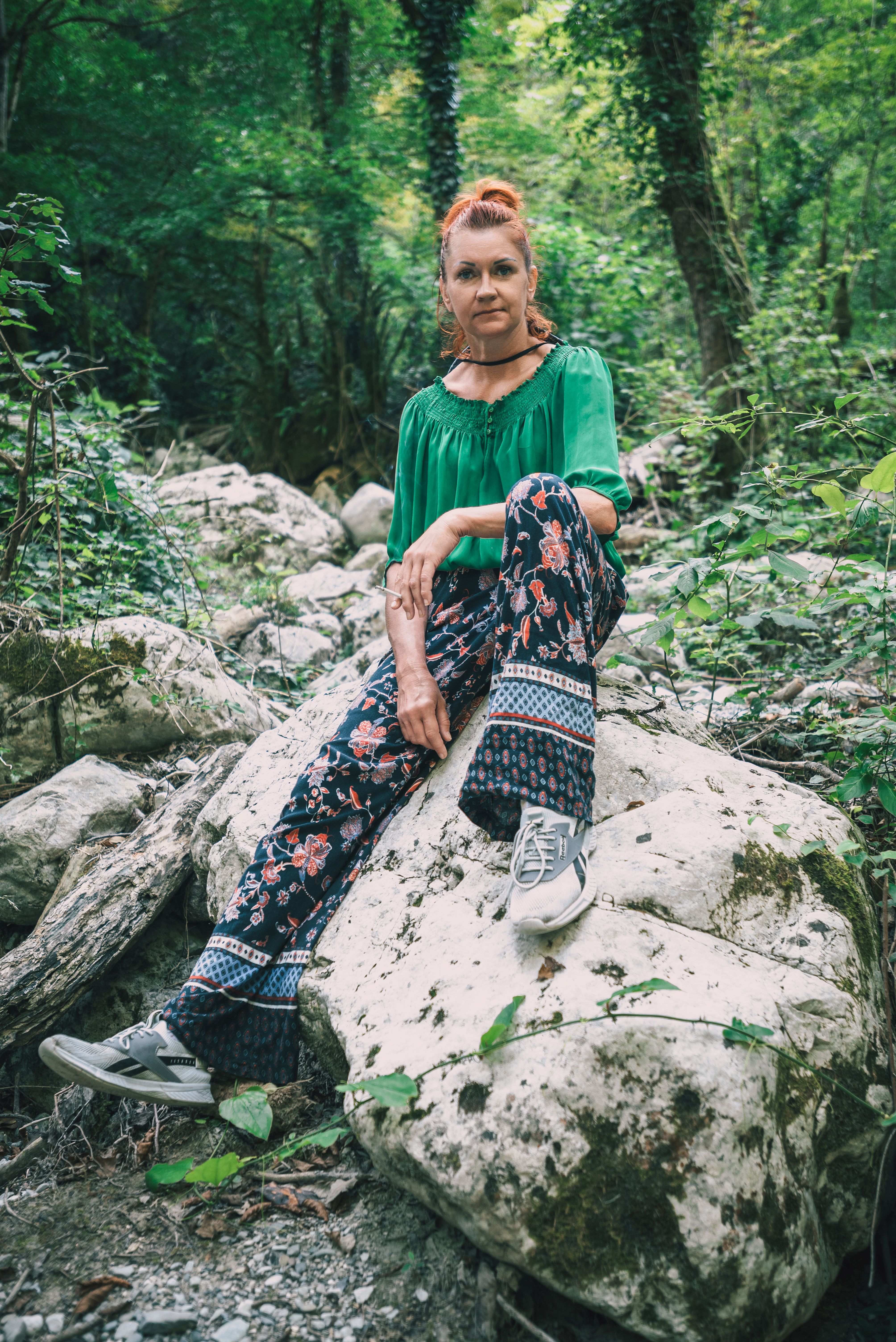 Casual portrait of a woman sitting on a rock in a lush forest in Гагра.
