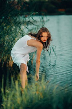 A young woman in a white dress standing in shallow water surrounded by greenery.
