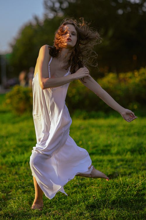 Free A woman dancing gracefully in a flowing white dress on a sunny day in a meadow. Stock Photo