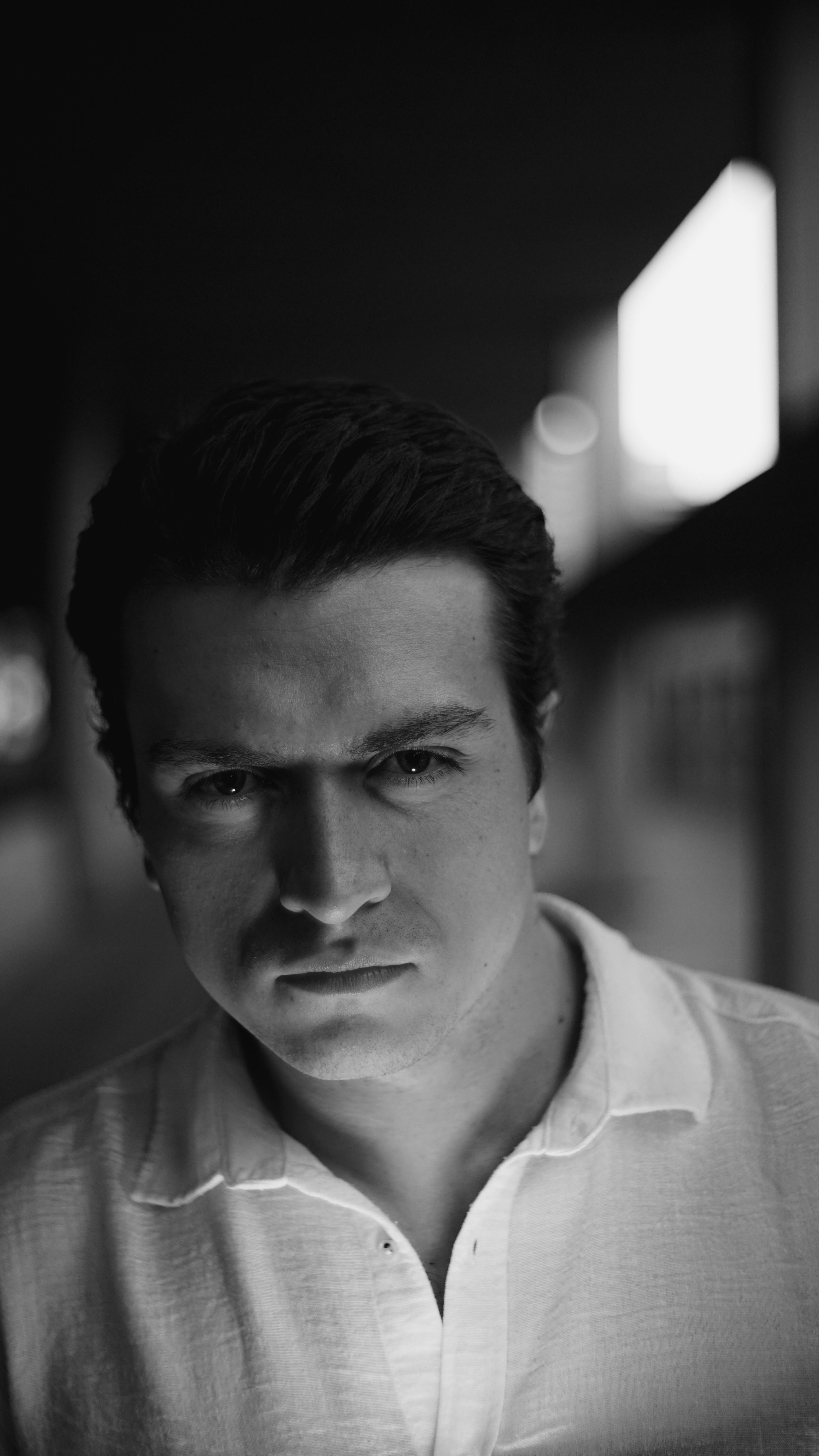 Moody black and white portrait of a man in a dimly lit environment.