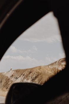 Brown desert hills viewed through car window, offering a serene natural scene.