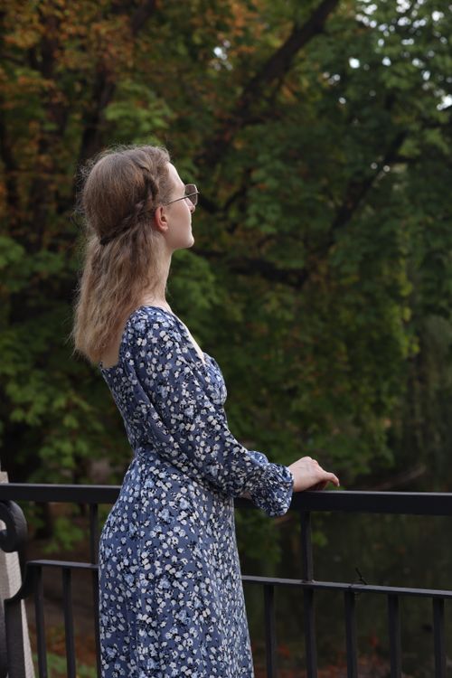 Free A serene scene of a woman in a floral dress enjoying a park view in Warsaw. Stock Photo