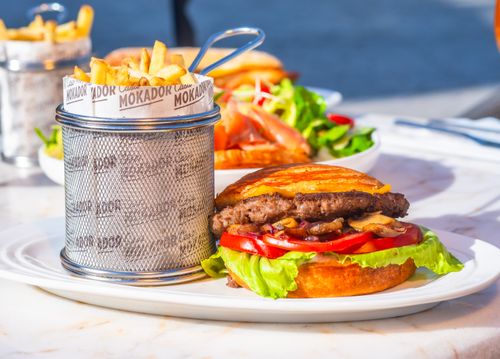 Free Mouth-watering burger with fresh lettuce, tomato, and fries served on a sunny outdoor table. Stock Photo