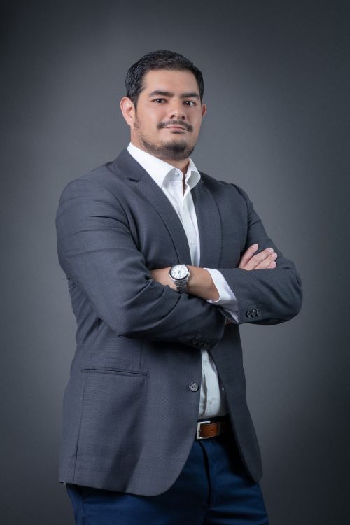 Free Portrait of a confident man in a gray business suit with arms crossed against a gray background. Stock Photo