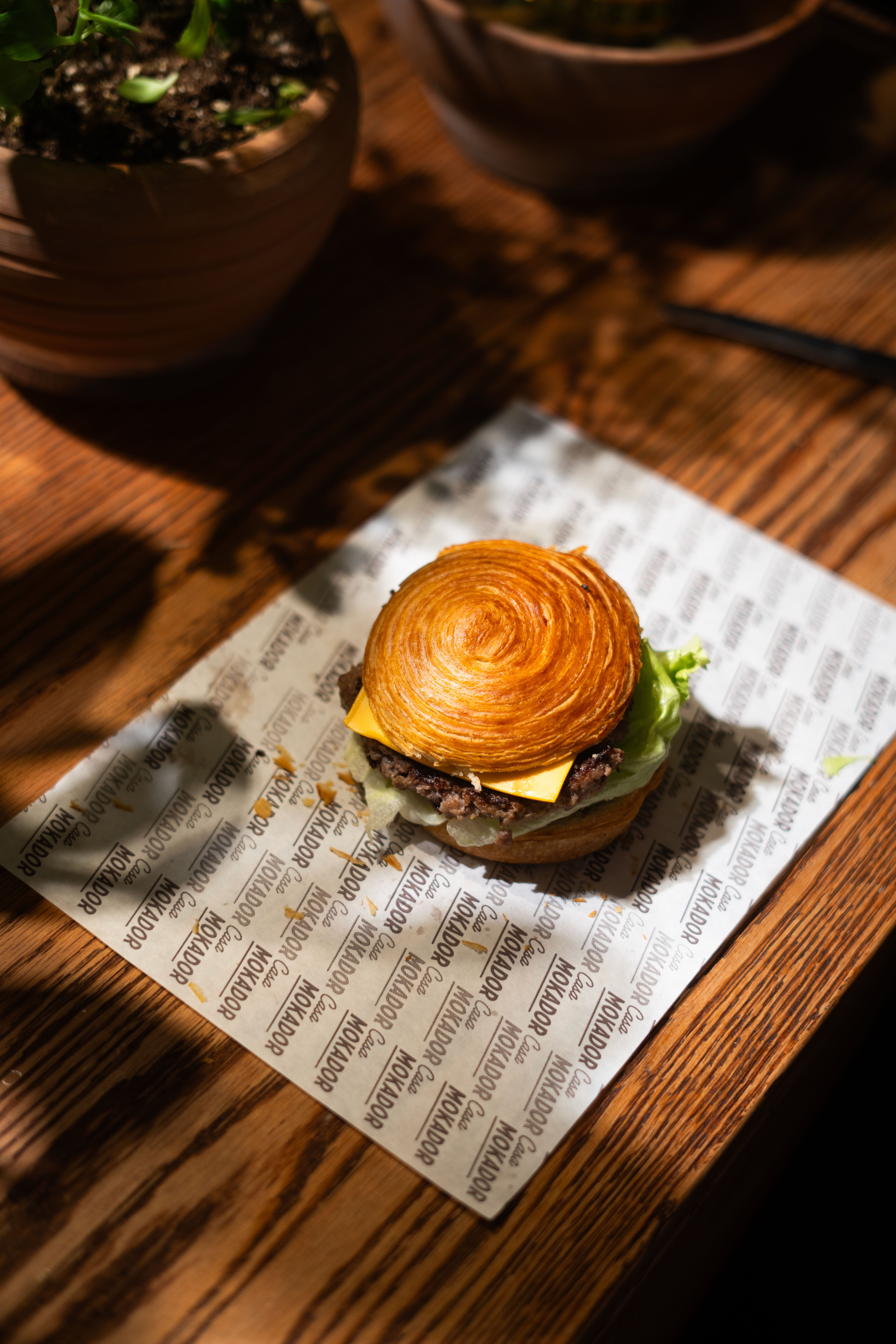 A close-up view of a gourmet burger with cheese and lettuce on a wooden table.