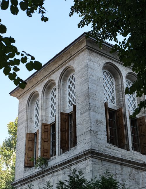 Free Historic stone building with elegant arches and wooden shutters in lush greenery. Stock Photo