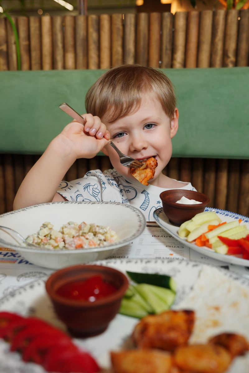 A young child happily eating a meal with fresh vegetables and dip.