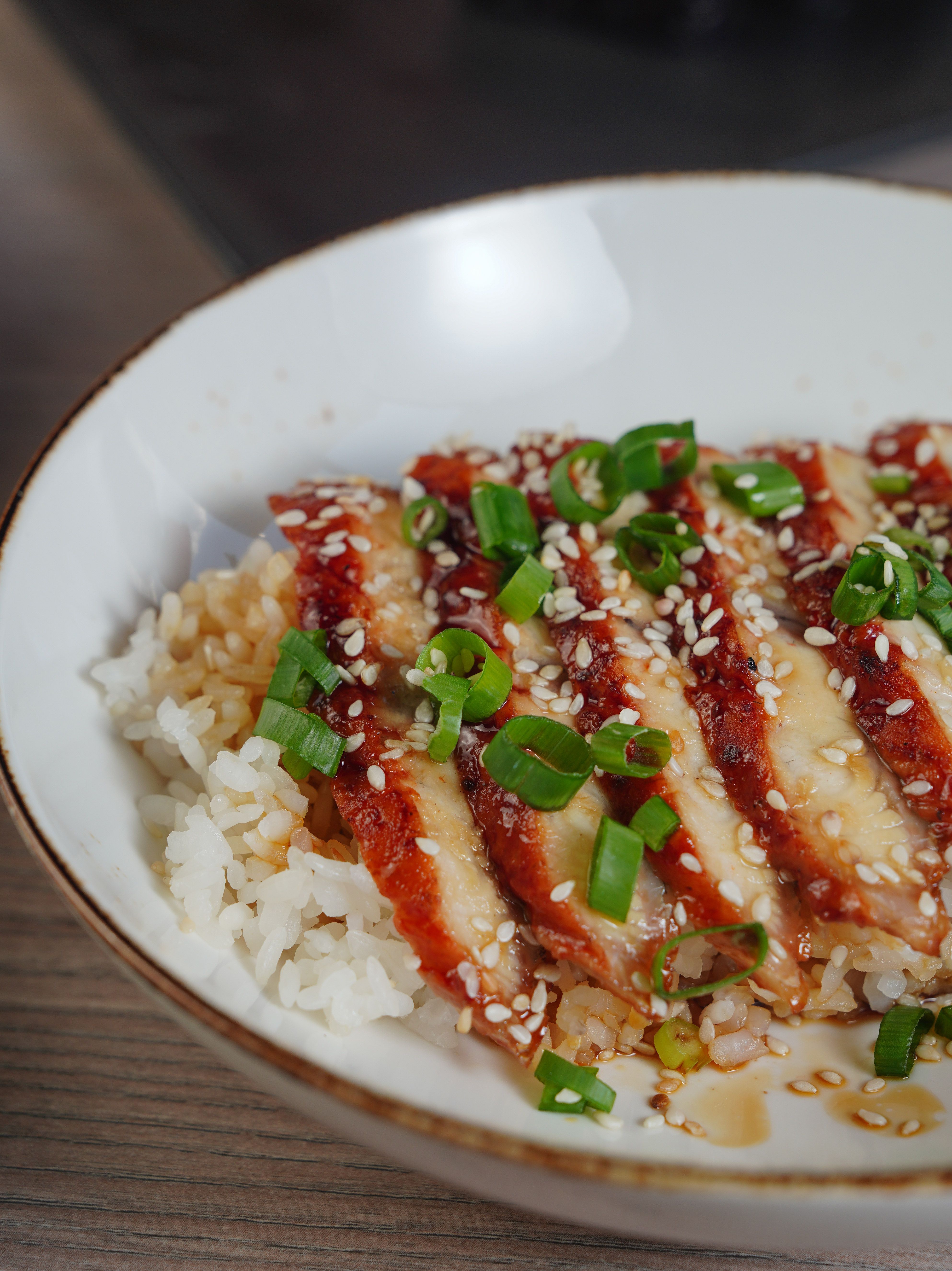 A teriyaki chicken rice bowl topped with sesame seeds and green onions