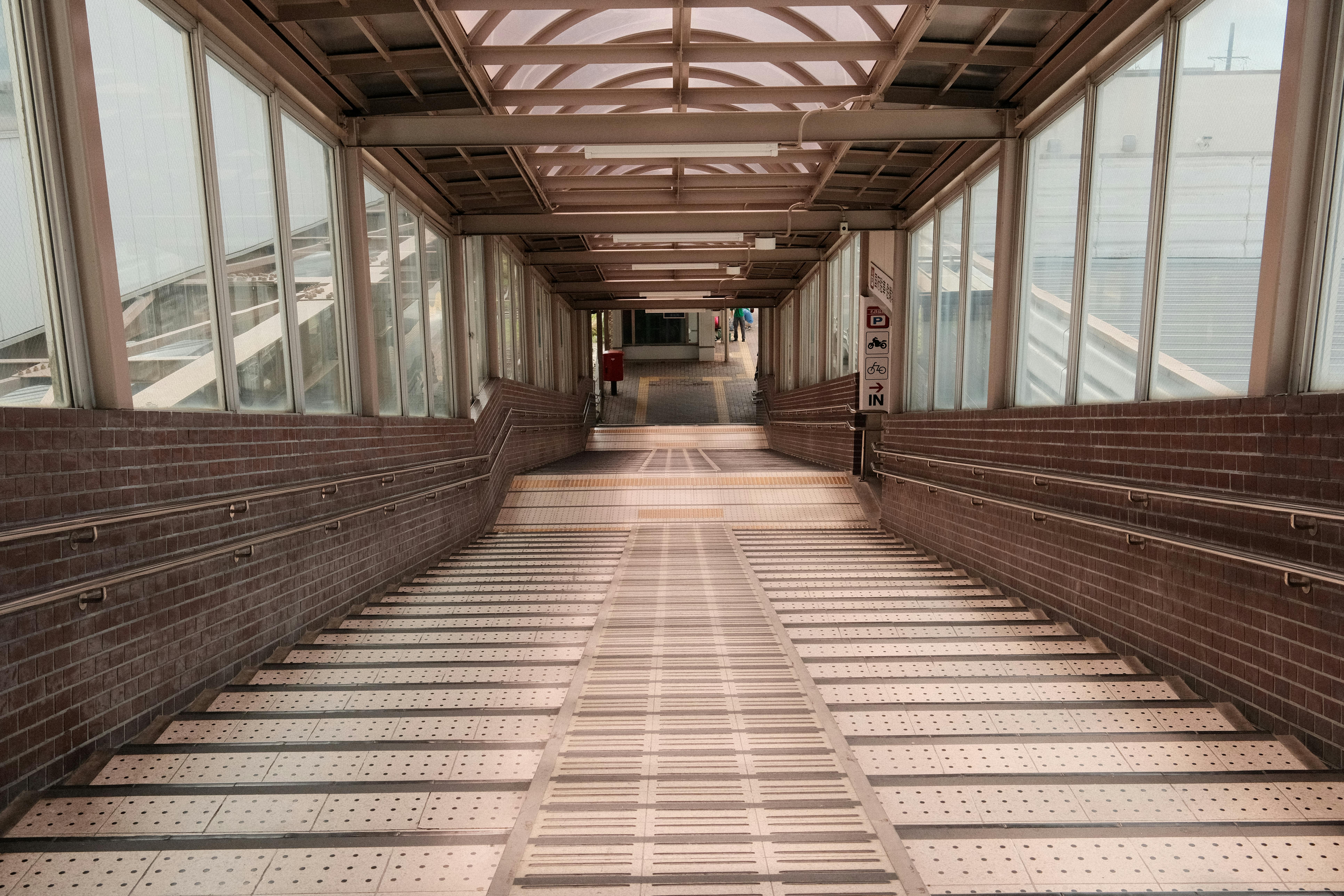 Empty corridor in Toyokawa train station with glass walls and tiled floor, Japan.