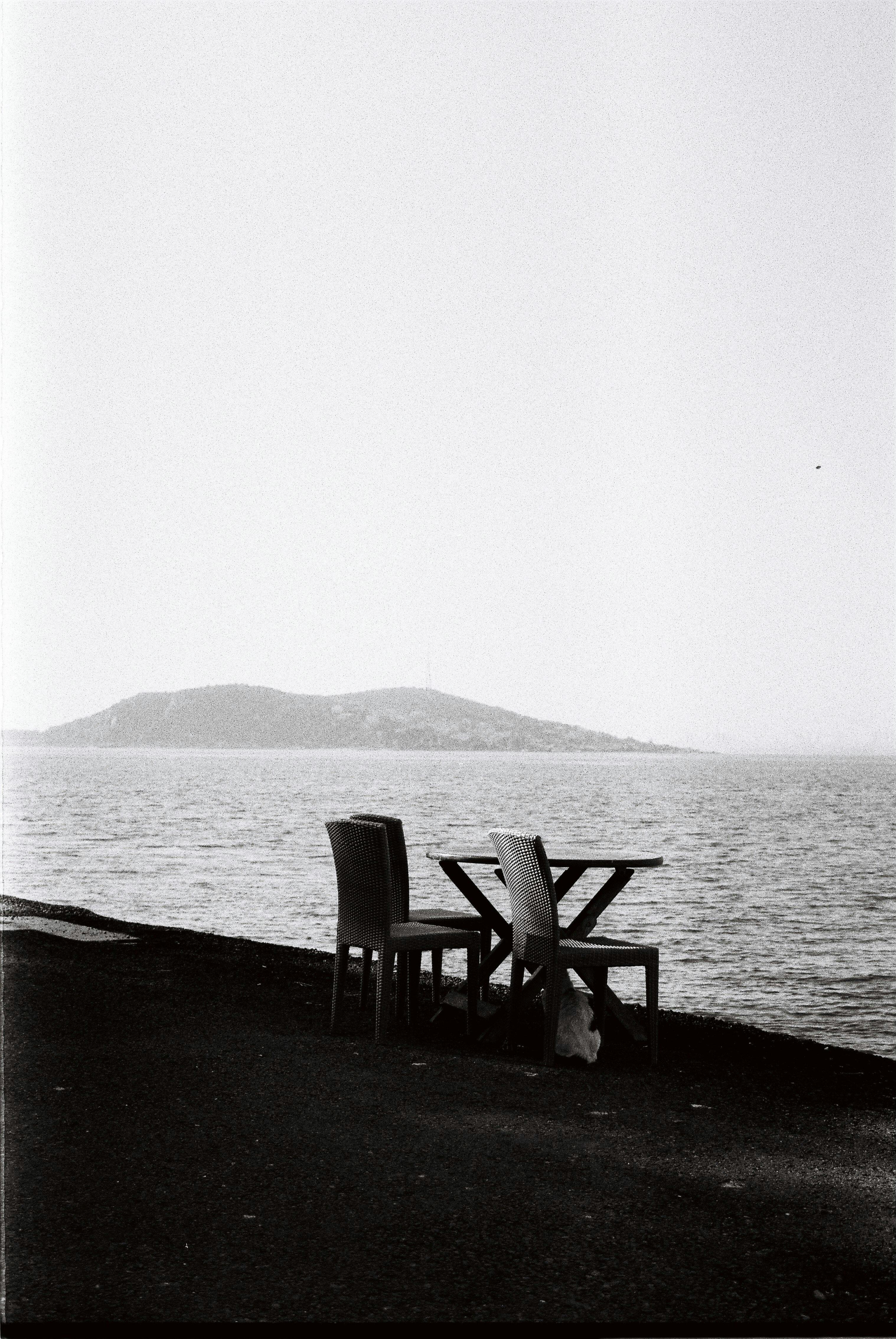 Empty chairs by the sea with distant island in monochrome.