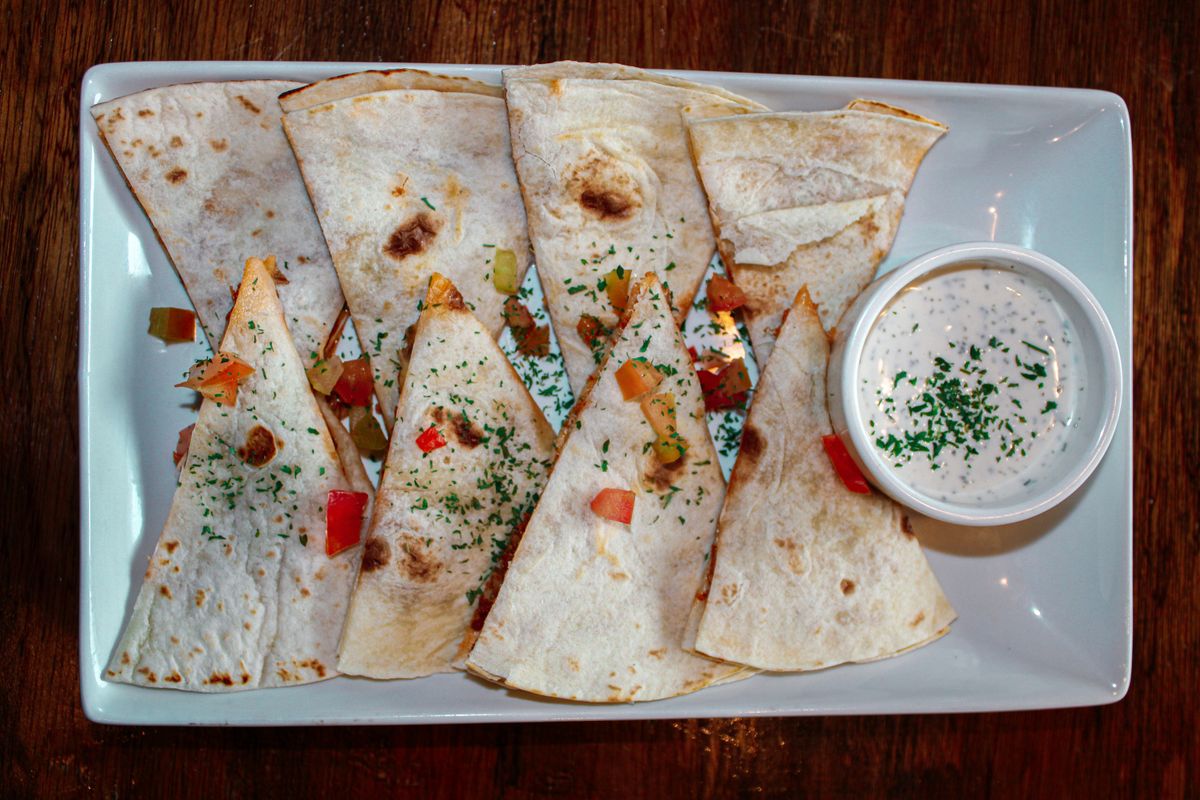 Flour tortilla quesadilla wedges with red pepper and chicken, sprinkled with parsley, and ranch dip