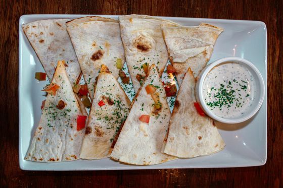 Flour tortilla quesadilla wedges with red pepper and chicken, sprinkled with parsley, and ranch dip