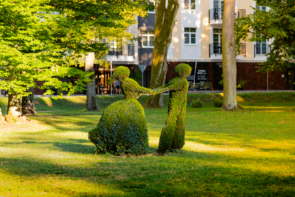 Two topiary sculptures resembling a dancing couple in a sunny park setting.