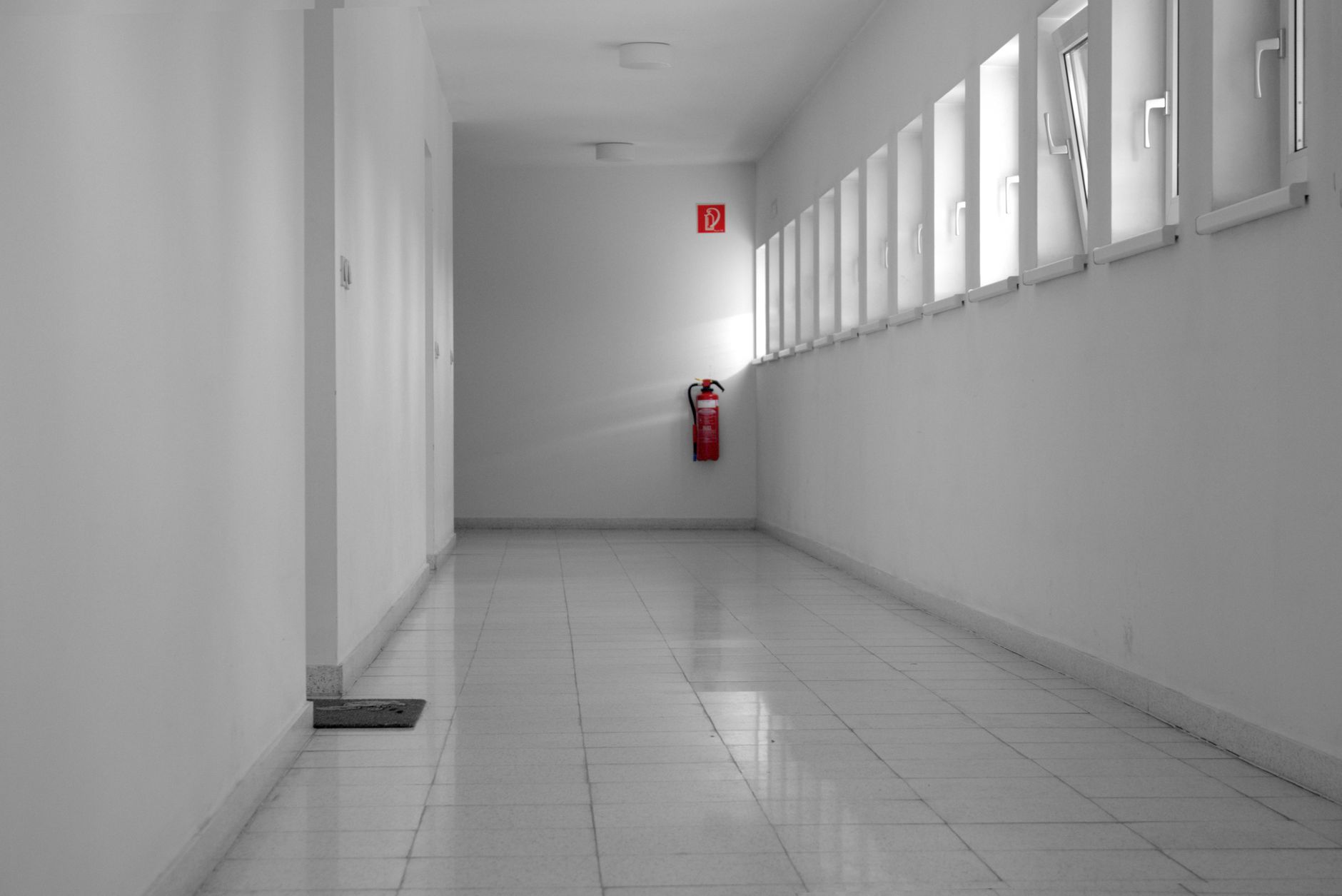 A sleek white corridor featuring a single red fire extinguisher on one wall.