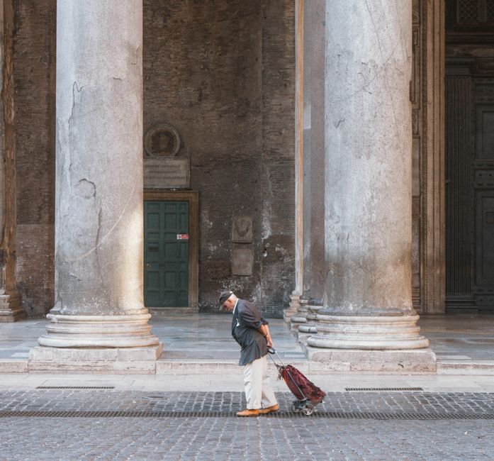 Elderly man with suitcase walking past large columns in Rome. Urban scene in Italy.