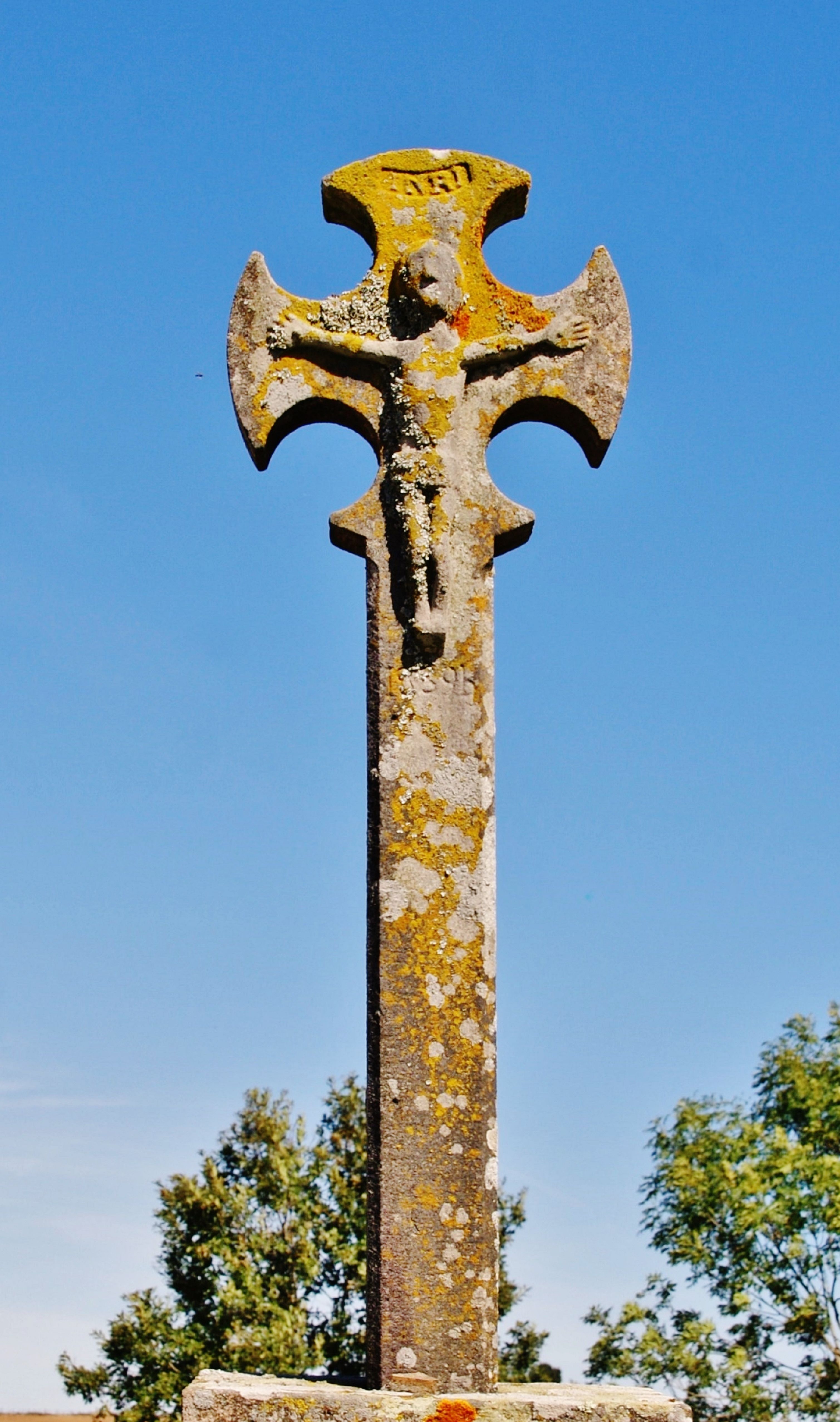 A weathered stone calvary cross stands against a clear blue sky, symbolizing history and spirituality.