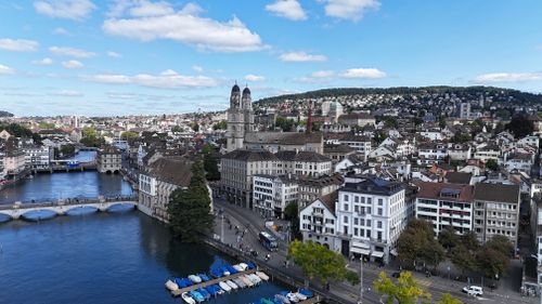 Free Aerial cityscape of Zurich, showcasing historic architecture, river, and Limmatquai under a vibrant blue sky. Stock Photo