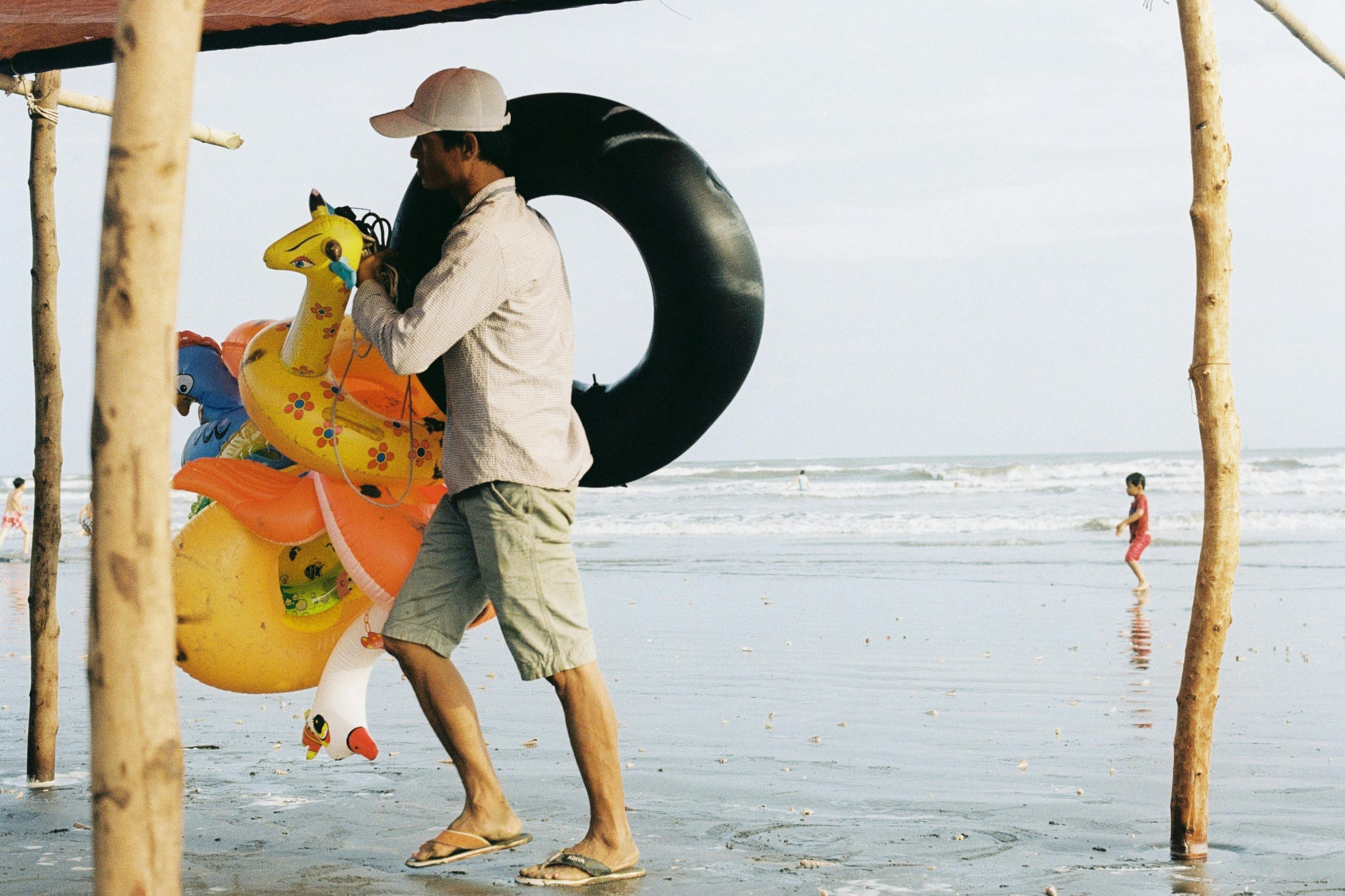 A vendor carrying inflatable toys on a lively beach in Ho Chi Minh City, Vietnam.