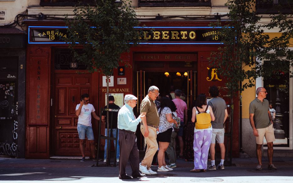 Personas reunidas fuera de la Taberna Alberto en Madrid, España, capturando la vida callejera local.