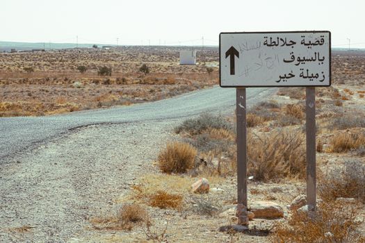 Directional sign on a desert road in Tataouine, Tunisia with Arabic text.
