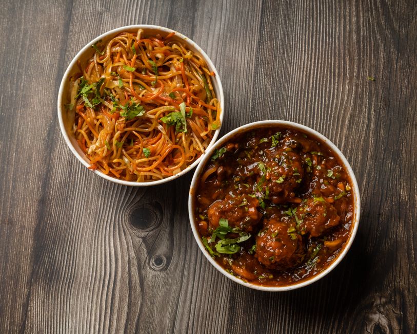 Tantalizing two dish combo of noodles and Manchurian on a wooden background, perfect for a flavorful meal.