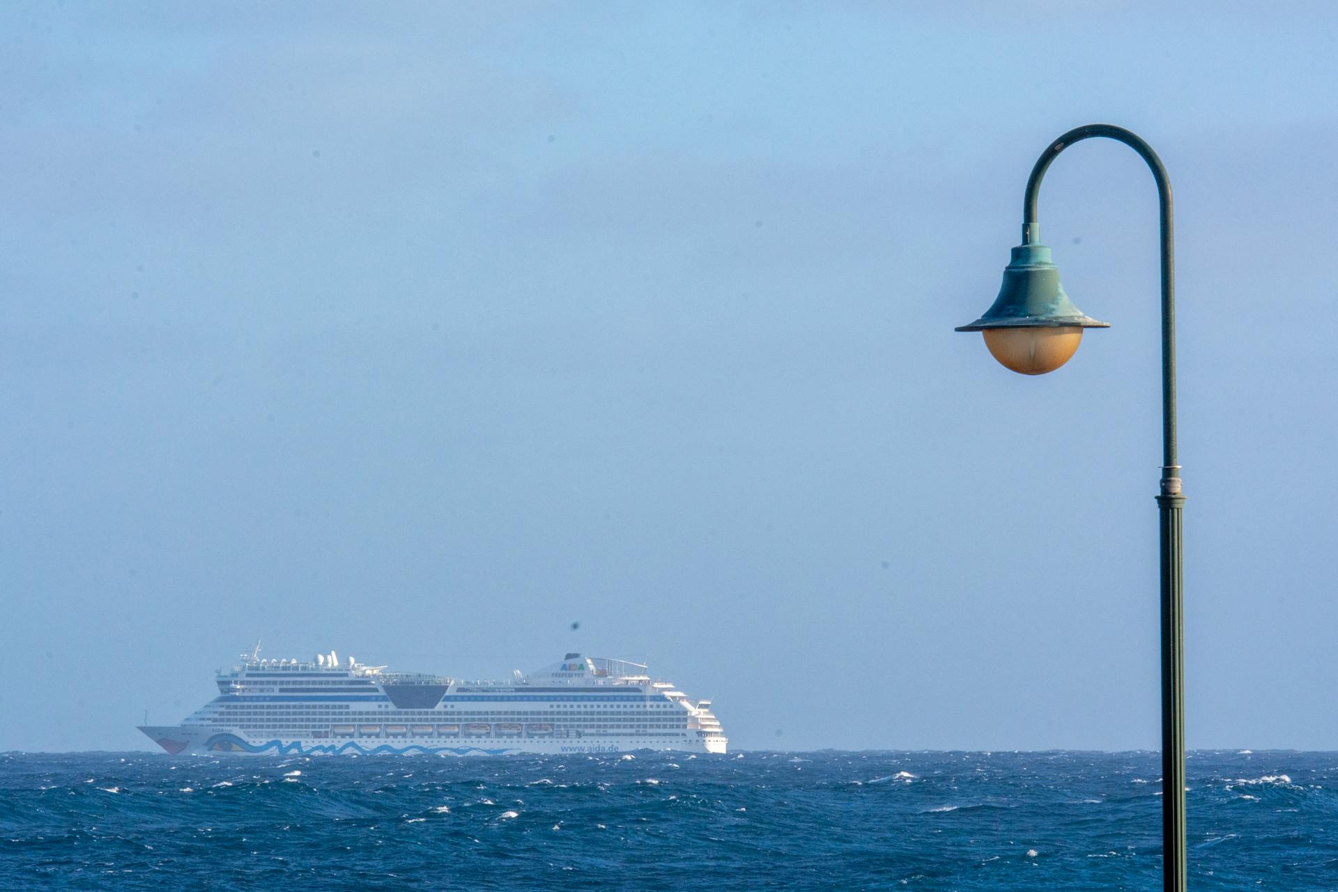 A scenic view of a cruise ship on the ocean with a street light in the foreground under a clear sky.