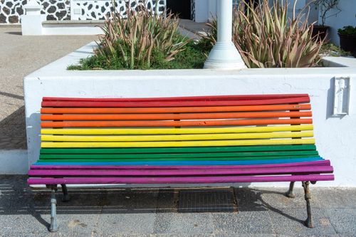 Free Vibrant rainbow-colored bench in a bright urban outdoor setting with plants. Stock Photo