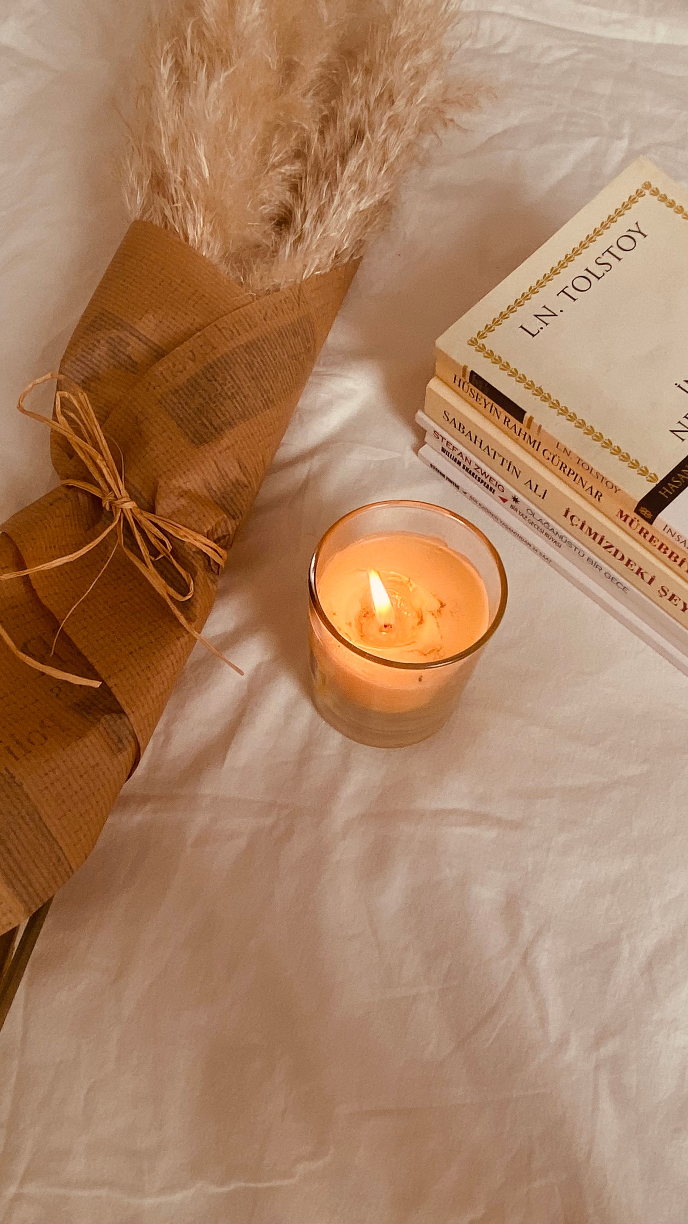 Candlelit scene with wrapped flowers and classic books on soft fabric.