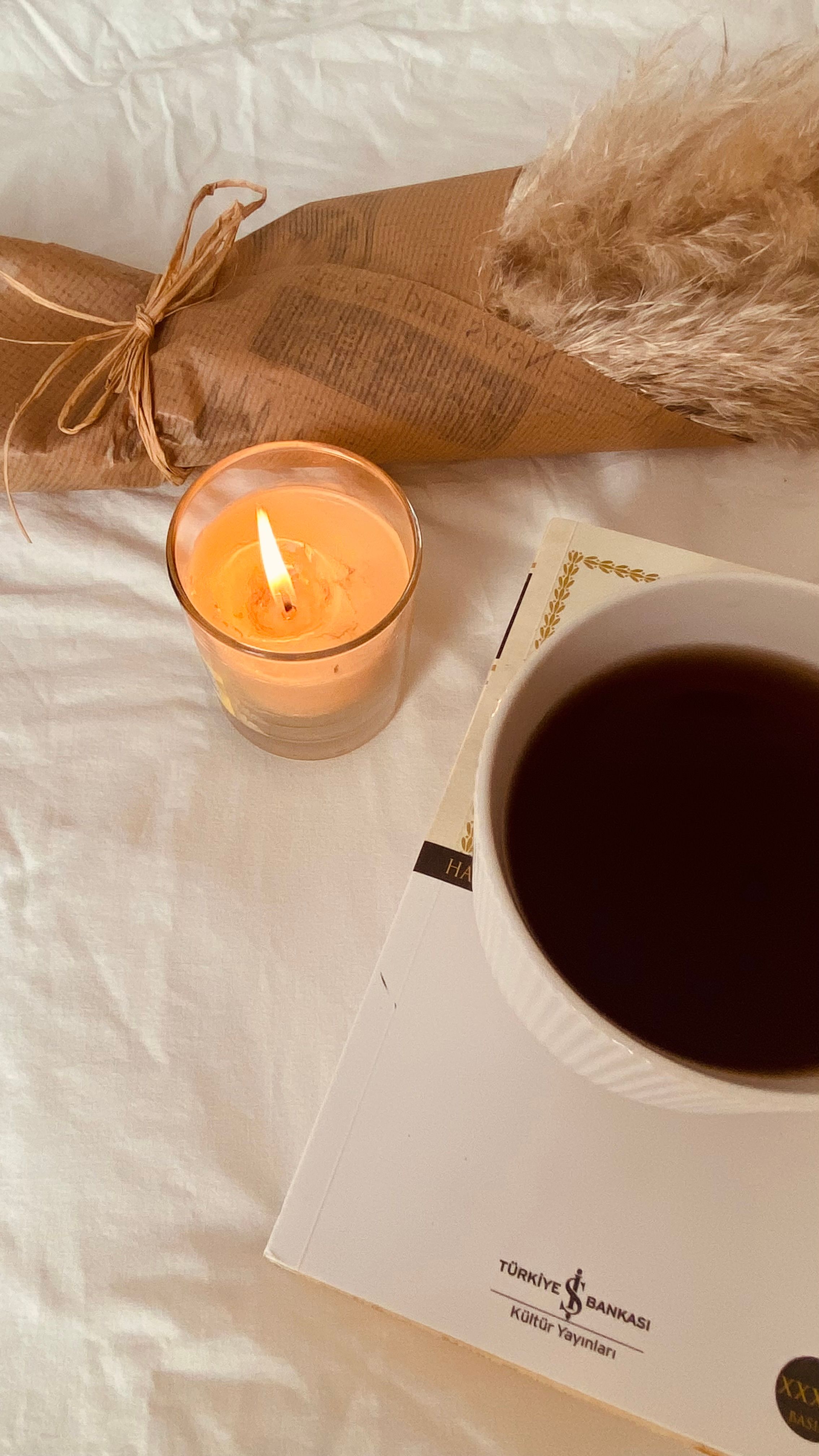 Free Warm flat lay of coffee, candle, and book on white fabric. Stock Photo