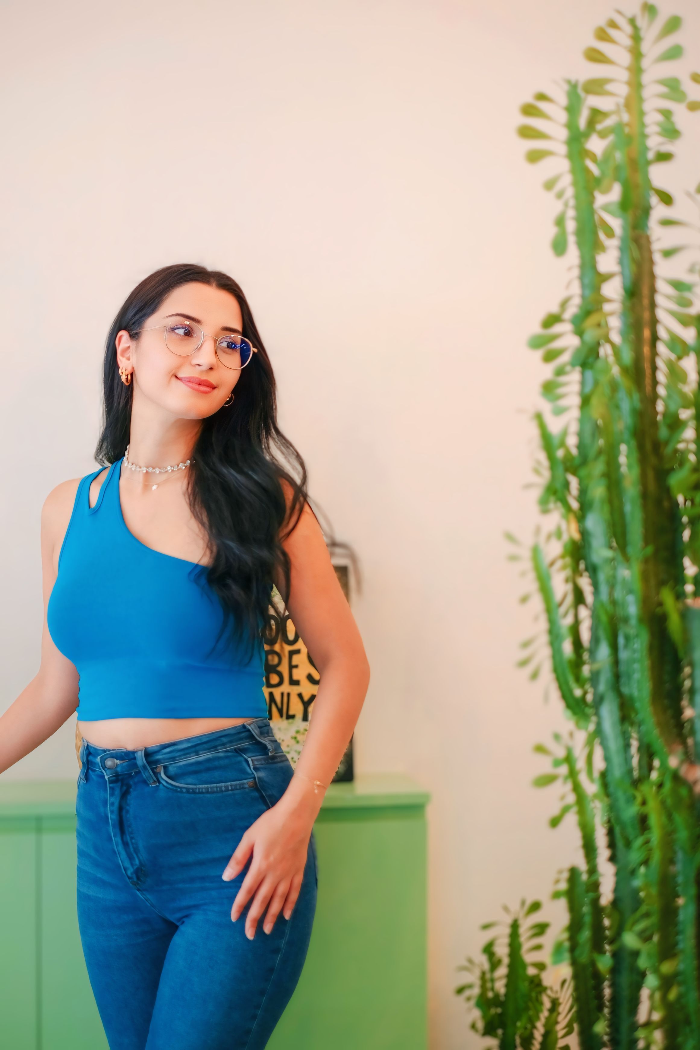 Woman in blue top standing beside indoor plants, cheerful ambiance.