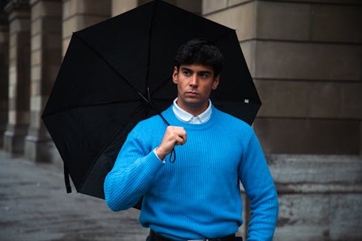 Stylish man in blue sweater with umbrella on a rainy day in Munich, street setting.