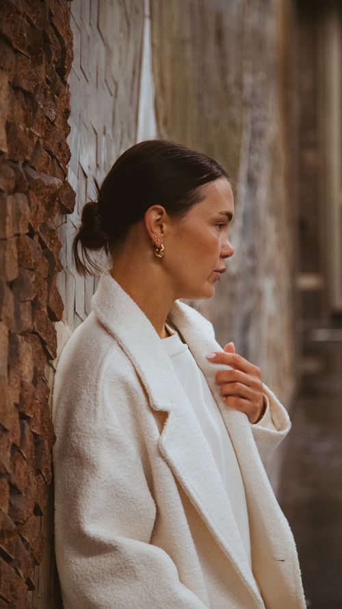 Free Thoughtful woman in a stylish coat stands in a Munich alley on a rainy day. Stock Photo