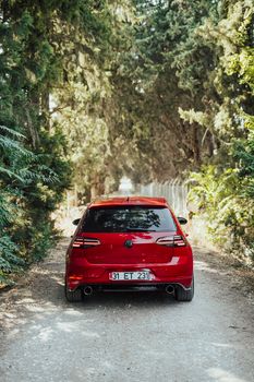 A red Volkswagen Golf GTI parked on a scenic, tree-lined path during daytime.