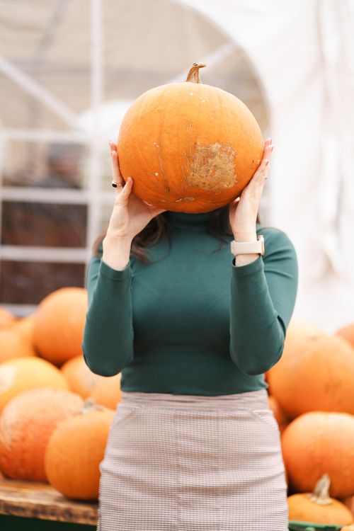 Free A woman in a green sweater playfully holds a pumpkin in front of her face, surrounded by autumn pumpkins. Stock Photo