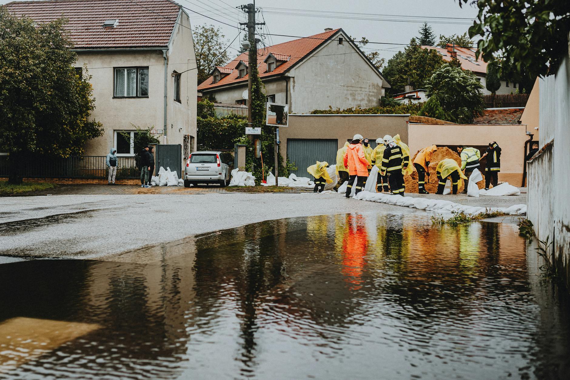 Emergency responders in reflective gear addressing floodwaters on a residential street.