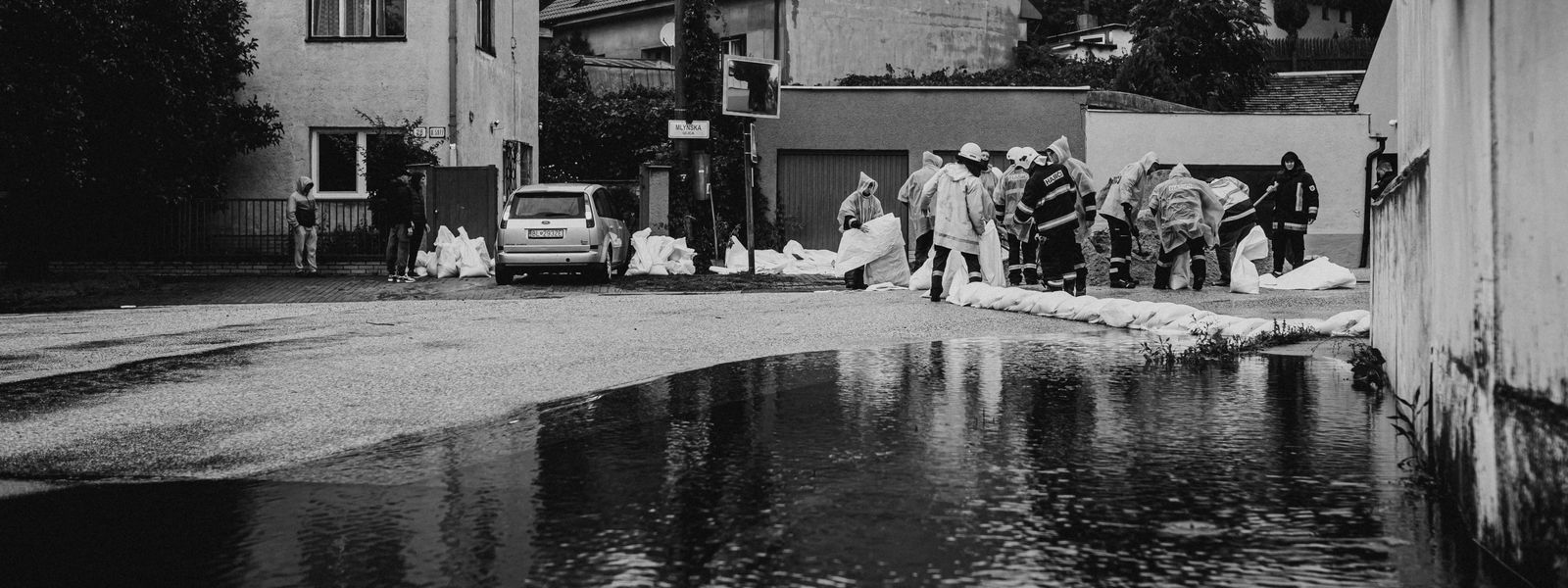Crews in rain gear building sandbag barriers in a flooded street